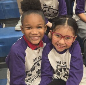 two girls in elementary school sit closely and smile at the camera