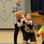 young girl on a basketball court getting ready to pass, with referee behind her